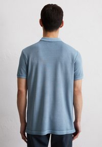 Lichtblauwe poloshirt van zachte stof, met een standaardkraag, korte mouwen en een rechte zoom met minimale details.