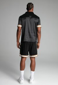 Polo shirt in mesh nera con maniche bordate d'oro, abbinato a pantaloni corti neri con strisce dorate. Tessuto liscio, vestibilità rilassata.