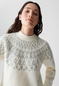 Maglione bianco in lana con scollo rotondo, caratterizzato da un colletto grigio a fantasia e un tessuto morbido e testurizzato. Vestibilità rilassata e maniche lunghe.