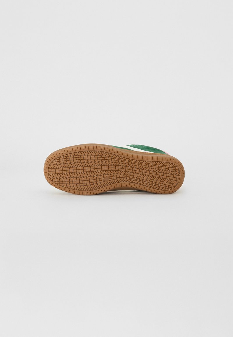 Baskets vertes et blanches avec une tige lisse, une semelle en caoutchouc texturée et crantée, et des détails de couture contrastants. Semelle extérieure en caoutchouc visible.