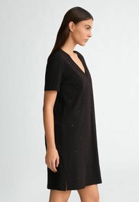 Rochie neagră cu mâneci scurte și decolteu în V, cu accente decorative din metal negru și fente laterale, realizată dintr-un material neted.