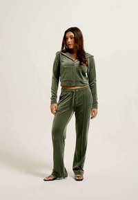 Fato de veludo em verde oliva, com uma hoodie curta de fecho e calças com cordão. Apresenta um bolso frontal e uma silhueta ajustada.
