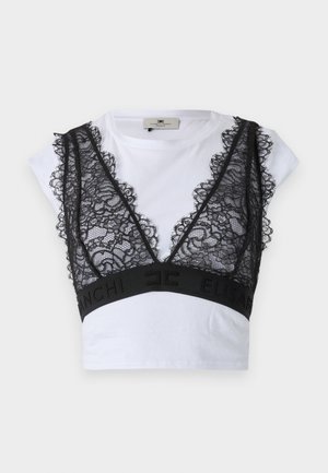 Svart blonder bralette med scallopede kanter over en hvit T-skjorte med korte ermer; har et svart elastisk bånd med merkevare.
