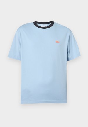 Lichtblauw T-shirt met korte mouwen en een zwarte kraag, met een klein oranje krokodillenlogo op de linkerborst, tegen een witte achtergrond.