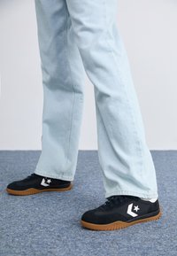 Baskets en daim noir avec une semelle en caoutchouc, arborant un logo d'étoile blanche et des accents sur le côté. Associées à un pantalon en denim bleu clair.