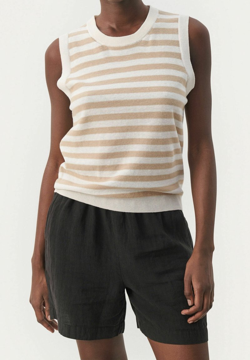 Personne portant un haut en maille sans manches à rayures horizontales beige et blanche avec des bords côtelés et un short ample noir.