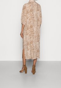 Abito beige a fantasia con macchie di leopardo marroni, maniche corte, spacco laterale e colletto, abbinato a sandali alti color nocciola.