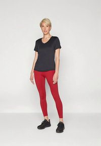 Maglietta atletica nera a maniche corte, abbinata a leggings rossi e scarpe da ginnastica nere. Presenta un design con scollo a V e una silhouette aderente.