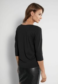 Czarna bluzka z rękawem trzy czwarte, o luźnym kroju, z szerokim dekoltem i gładką fakturą. W zestawie z dopasowaną czarną spódnicą skórzaną.