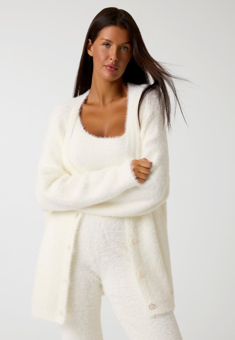 Cardigan bianco e morbido con chiusura a bottone, abbinato a un top coordinato. Entrambi i capi hanno una consistenza morbida e una vestibilità rilassata.