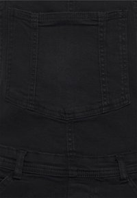 Mustat farkkuhaalarit sisältävät suuren suorakulmaisen takataskun, erottuvan ompeleen ja tukevat hihnat turvallista käyttöä varten.