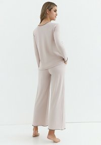 Jasnoróżowy komplet piżamowy z długim rękawem, top z okrągłym dekoltem oraz szerokimi spodniami, wykonany z miękkiego materiału z kontrastową czarną lamówką.