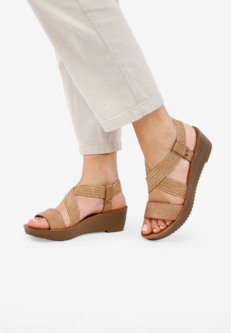 Sandalias de cuña en tono beige con diseño de tiras cruzadas, fabricadas con material sintético. Las correas texturizadas y una suela de goma sólida ofrecen estabilidad.