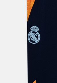 Navy jersey with orange accents, featuring a light blue Real Madrid logo and crown. Fabric appears smooth with contrasting textured patterns.