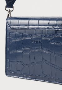 Tumedate krokodillimustriga nahkrahakott, millel on sile tekstuur, lame disain ja diskreetne logo. Omab eemaldatavat rihma ja hõbedast stiilset riistvara.