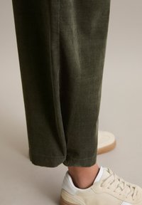 Olivgrüne Cord-Hosen mit lockerer Passform und Umschlagsaum, kombiniert mit weißen und beigen Sneakers mit strukturierter Sohle.