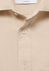 Beige linen blend shirt featuring a pointed collar, button closure, and textured fabric. Label reads "Linen Blend."