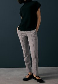 Pull noir à manches courtes associé à un pantalon à carreaux gris clair avec des bandes latérales, et des ballerines noires. Design simple et ajusté.
