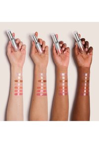 Drie handen houden zilveren lipgloss-tubes boven swatches van verschillende tinten op armen. De swatches variëren van nude tot roze en benadrukken verschillende huidskleuren.