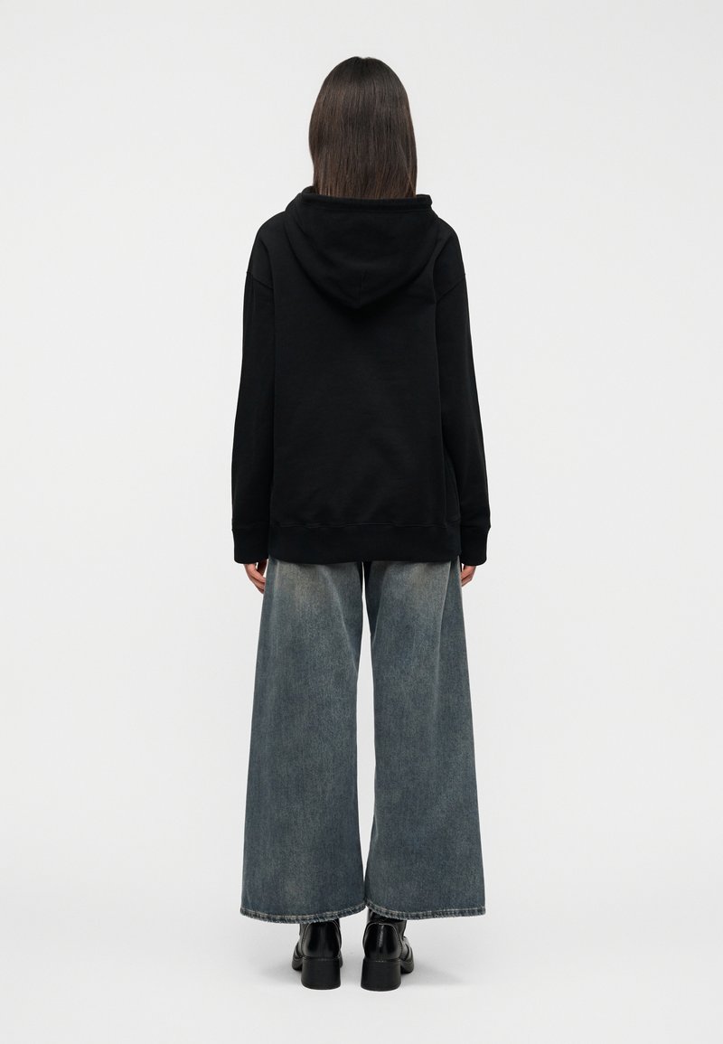Black hooded sweatshirt with a relaxed fit, paired with wide-leg blue denim jeans and black chunky heeled boots. Back view.