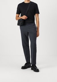 Svart t-shirt matchad med mörka, strukturerade byxor och svarta skor. Väskan är svart med en axelrem. Enkel och funktionell design.