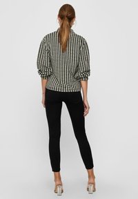 Blouse à motif pied-de-poule noir et blanc avec manches bouffantes, associée à un jean noir skinny et des sandales à talons blocs transparents.