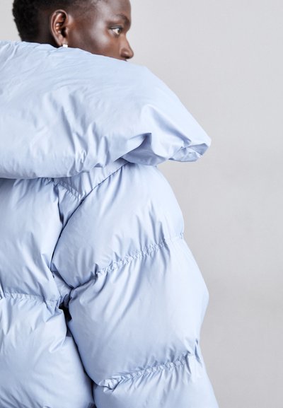 Lichtblauwe gewatteerde jas met een hoge kraag en een oversized capuchon. Kenmerkt zich door een gewatteerde textuur en een elastische zoom voor een strakke pasvorm.