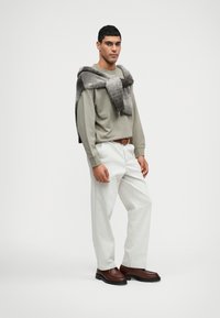 Světle šedý svetr, béžové kalhoty, hnědý opasek a tmavě hnědé boty. Po ramenou je přehozená texturovaná šedá šála.