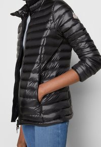 Sort dunjakke med blank finish, med vandrette quiltede sektioner, høj krave og sidelommer. Lynlåslukning synlig.