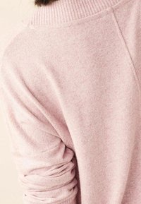 Weicher rosa Strickpullover mit einem gerippten Rollkragen und leicht umgeschlagenem Ärmel, gezeigt auf dem oberen Rücken und der Schulter einer Person.