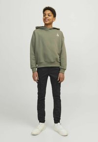 Sweatshirt à capuche vert olive avec un logo blanc, associé à un pantalon cargo noir et des baskets blanches, présentant une coupe décontractée et des poignets côtelés.
