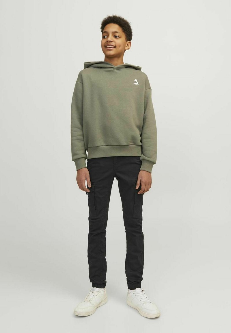 Sweatshirt à capuche vert olive avec un logo blanc, associé à un pantalon cargo noir et des baskets blanches, présentant une coupe décontractée et des poignets côtelés.