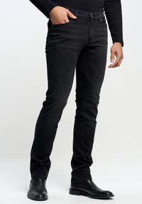Jeans in denim nero con vestibilità slim, caratterizzati da un design a cinque tasche, una texture sottile e una chiusura classica a bottoni. Indossati con stivaletti neri alla caviglia.
