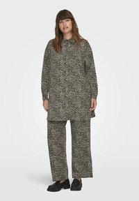 Tunis ir kelnių komplektas leopardų raštu, smėlio ir juodos spalvos, su ilgomis rankovėmis, apykakle ir laisvu siluetu. Stiliaus akcentas - juodi platforminiai batai.