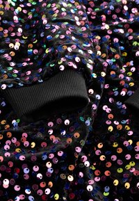 Tessuto nero ricoperto di paillettes multicolori; presenta polsini neri a coste. Superficie lucida e testurizzata con una qualità riflettente vibrante.