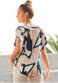 Kurzärmlige, locker sitzende Bluse aus leichtem Stoff. Abstraktes geometrisches Muster in Blau-, Beige- und Pastelltönen. Gerundeter Halsausschnitt.