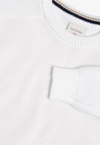 Hvid bomuldsstrik med en struktureret rund hals og ribbede ærmer. Har en diskret navy og beige stribe detaljer indeni halsudskæringen.