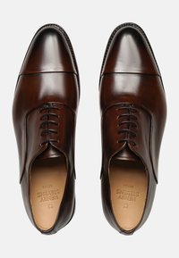 Scarpe eleganti in pelle marrone con un design elegante, caratterizzate da una punta chiusa, chiusura con lacci e una texture liscia. Presenti dettagli di cucitura sottili.