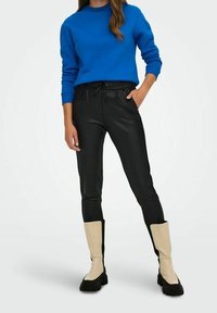 Felpa blu, pantaloni neri in ecopelle e stivali crema al ginocchio con dettagli neri. Design aderente con vita regolabile tramite cordoncino sui pantaloni.