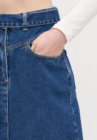 Blå denimskjørt med en frontlomme, med rett snitt og synlige sømdetaljer. Glatt tekstur med en avslappet passform.