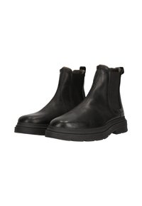 Ett par svarta läder Chelsea-boots med tjocka gummisulor och elastiska sidopaneler, visade på vit bakgrund.