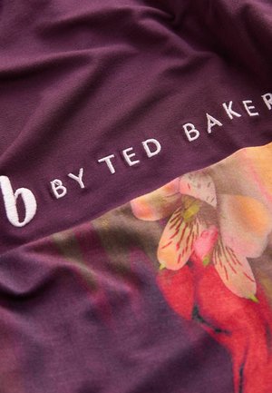 Violetti kangas, jossa on kukkakuvio ja valkoisella brodeeratut tekstit "b BY TED BAKER". Sujuva rakenne, jossa on eloisia värejä ja kuvioita.
