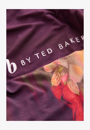 Tissu violet avec un motif floral et un texte brodé blanc indiquant "b BY TED BAKER." Texture lisse avec des couleurs et des motifs vibrants.