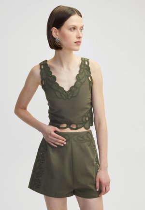 Olivově zelený crop top s propracovanými háčkovanými detaily a výřezovými prvky, doplněný o odpovídající šortky se podobnými dekorativními akcenty.