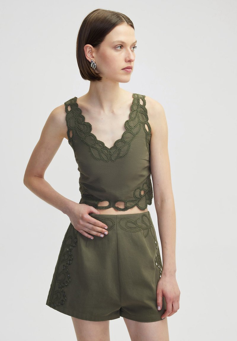 Top corto verde oliva con intrincados bordes de ganchillo y detalles cortados, combinado con pantalones cortos a juego que presentan acentos decorativos similares.