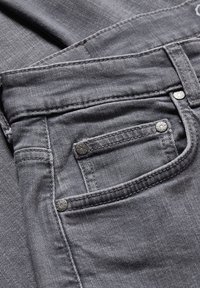 Jeans de mezclilla gris con un bolsillo frontal con remaches de metal, textura sutil y detalles de costura. La tela presenta un acabado suave.