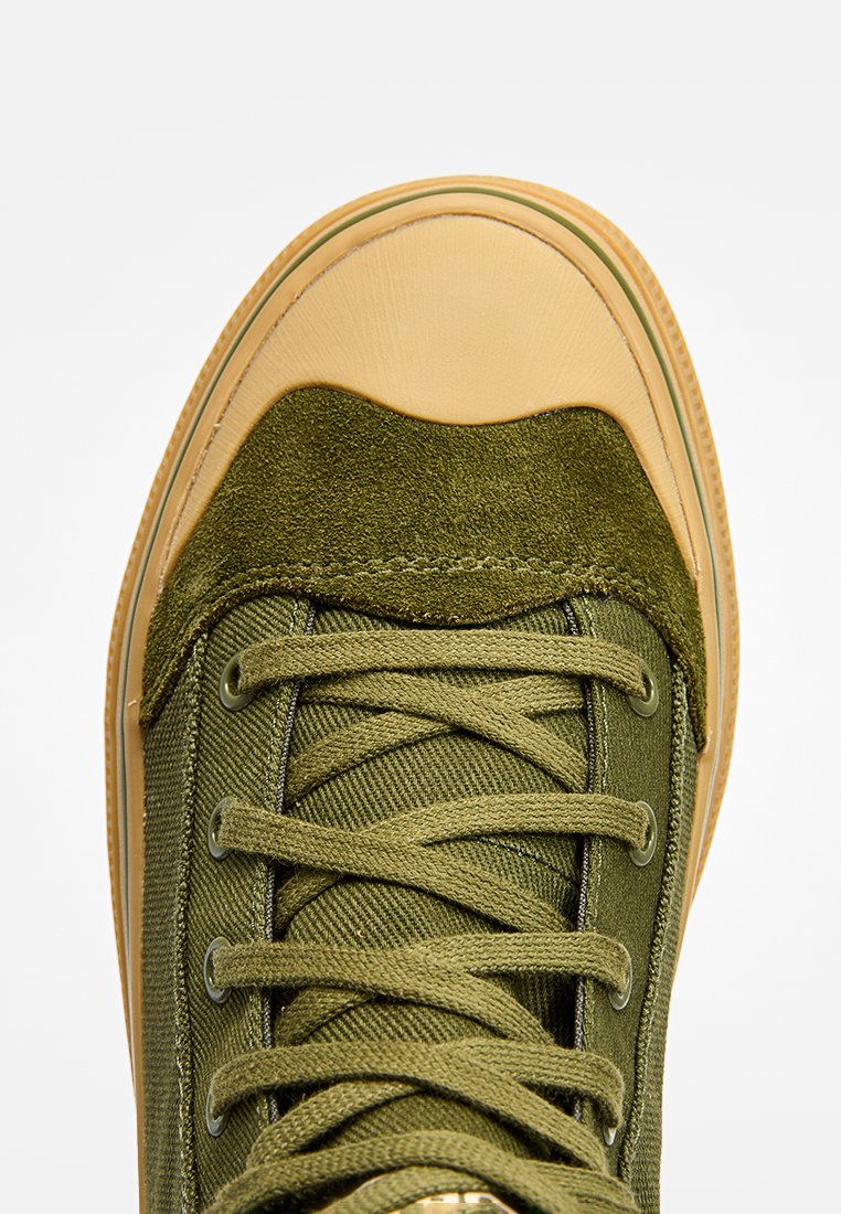 Grüne Canvas-Sneaker mit einer tanfarbenen Gummi-Zehenkappe, strukturiertem Textil-Obermaterial und kontrastierenden grünen Schnürsenkeln, ausgestattet mit einer glatten Sohle.