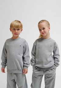 Graue Baumwoll-Sweatshirts mit langen Ärmeln und gerippten Bündchen, die mit einem kleinen Logo auf der Brust versehen sind, kombiniert mit passenden grauen Sweatpants.