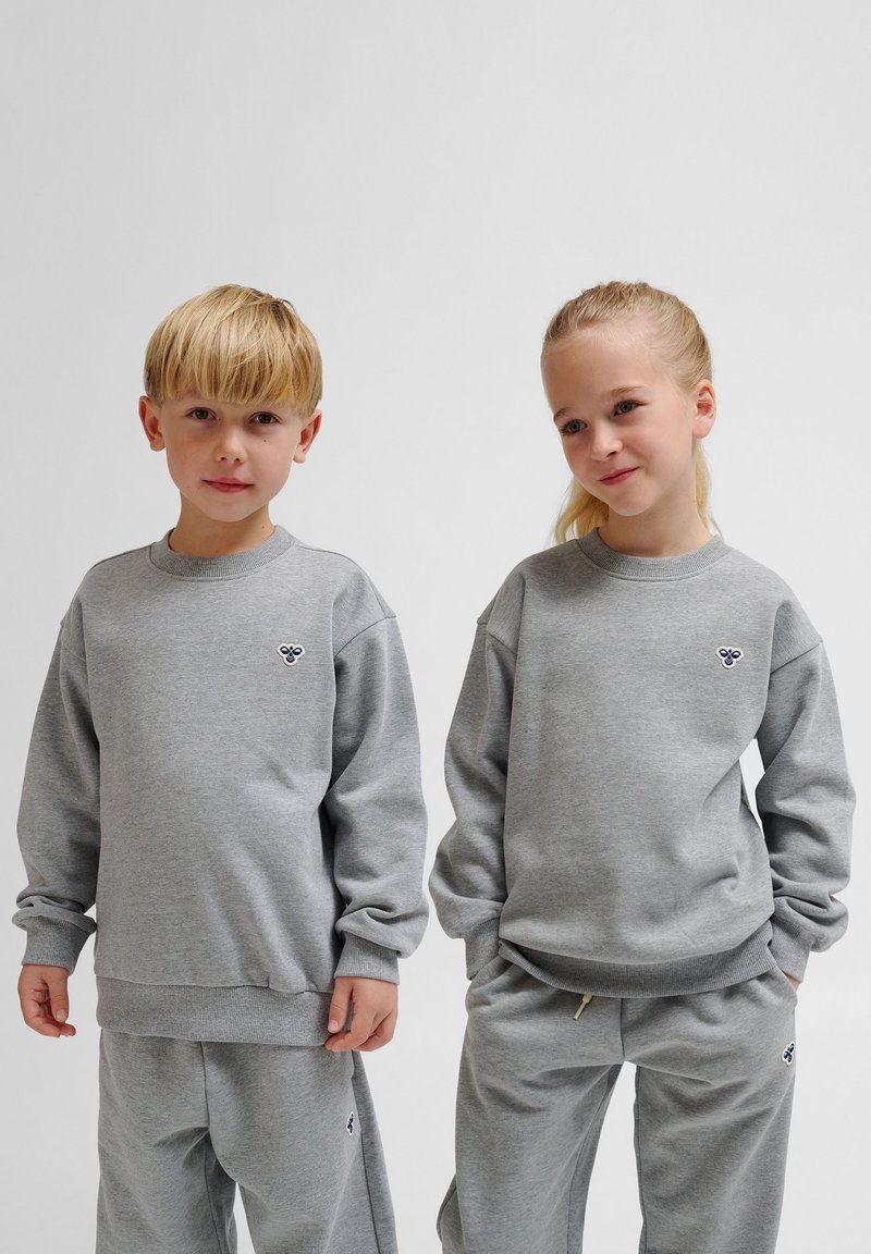 Graue Baumwoll-Sweatshirts mit langen Ärmeln und gerippten Bündchen, die mit einem kleinen Logo auf der Brust versehen sind, kombiniert mit passenden grauen Sweatpants.