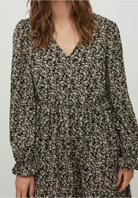 Blommönstrad klänning med svart bakgrund, prydd med små krämfärgade och rosa blommor, långa ärmar och V-ringning med rynkdetalj.